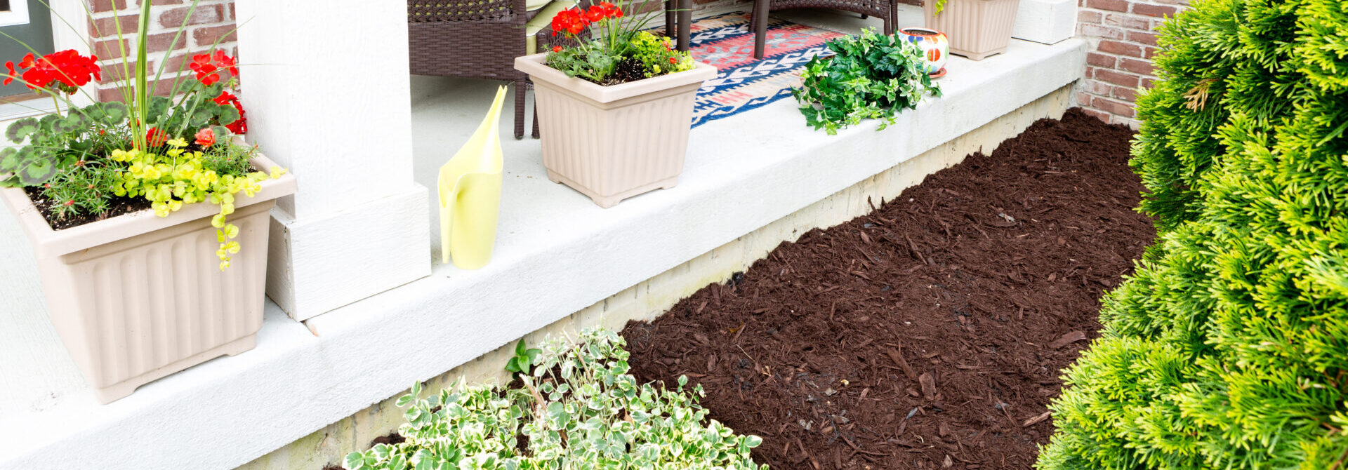 brown Mulching flowerbeds around the house with a freshly mulched bed alongside an open-air patio decorated with ornamental flowers